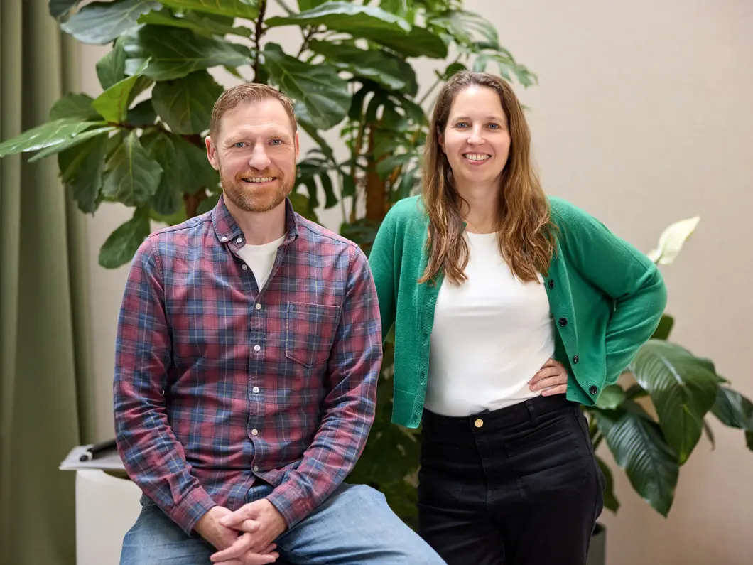 Andy and Alice side by side in front of a large leafy houseplant